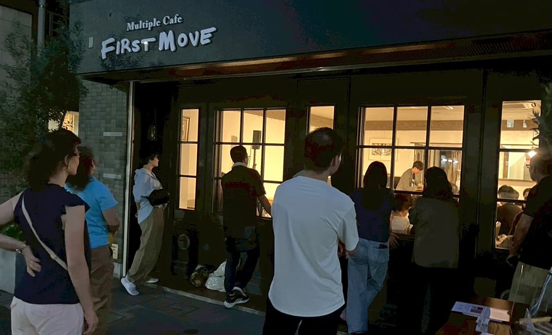 Menschen in Japan stehen vor dem FIRST MOVE Cafe und blicken auf eine lebhafte evangelistische Trickshow-Veranstaltung bei Nacht.