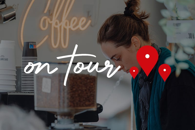 Eine Frau arbeitet an einer Kaffeetheke; im Tour-Modus werden das Bild mit Text und roten Standort-Pins überlagert.