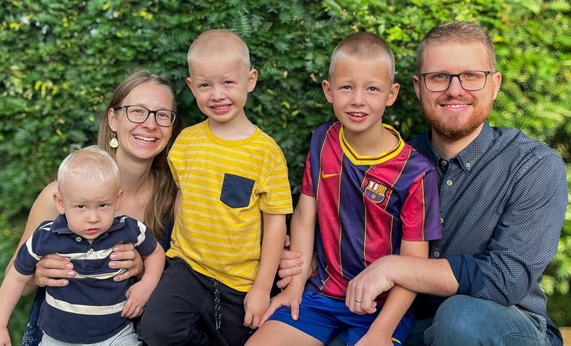 Eine vierköpfige Familie, die draußen vor einer Hecke für ein Foto posiert.